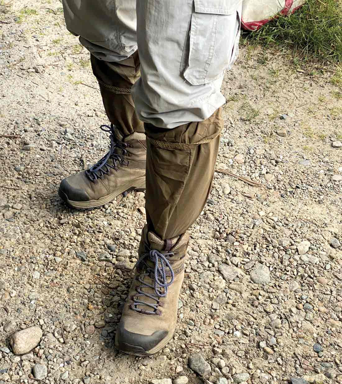 Person wearing Ticktogs with hiking boots and beige pants on a gravel path.